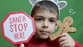 Cute boy with christmas sweater and deer alntlers holding sign Santa stop here and gingerbread man. Isolated on green Royalty Free Stock Photo