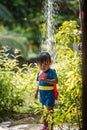 A cute boy dressed as superman showers in the garden
