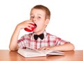 Cute boy eating apple while sitting at table isolated. Royalty Free Stock Photo