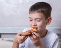 Cute boy eating a slice of pepperoni and cheese pizza, the child closed his eyes in pleasure, close-up, copy space