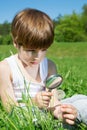 Cute Boy Examining Blossomed Flower Of Dandelion Thoroughly Through The Magnifying Glass While Sitting In The Grass Royalty Free Stock Photo