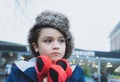 Cute boy with fluffy hat and warm jacket walking outside in the city, Kid with thinking face standing outside with blurry street Royalty Free Stock Photo