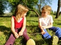 Cute boy and girl with blond hair are sitting on the grass and looking at each other. Kids in the field Royalty Free Stock Photo