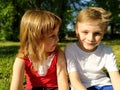 Cute boy and girl with blond hair are sitting on the grass and looking at each other. Kids in the field Royalty Free Stock Photo