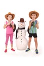 Cute boy and girl holding a cola bottle near a snowman with scarf and hat Royalty Free Stock Photo