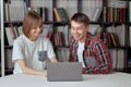 Cute boy and girl students working on a project in the city library, looking for books and typing notes on a laptop. Royalty Free Stock Photo