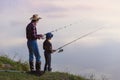 Cute 10-aged boy with his experienced grey-bearded 70-aged grandpa catching fish on the lake with landing net at sunset Royalty Free Stock Photo