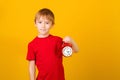 Cute boy holding red alarm clock. Time management concept. Schoolboy with retro clock isolated over yellow background Royalty Free Stock Photo