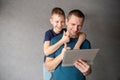 Cute boy hugs dad from behind, talking on a video link in a tablet Royalty Free Stock Photo