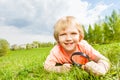 Cute boy with magnifier laying on the green grass