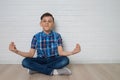 Cute boy is meditating and smiling while sitting in lotus position on the floor, copu space is availabe.