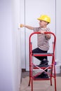 Cute boy with a paint roller. Happy kid helps parents to paint wall. Home renovation