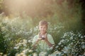Cute boy photographer shoots on camera in nature. Kid takes a photo in the camomile flowers field Royalty Free Stock Photo