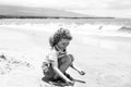 Cute boy playing with sand on summer tropical beach. Happy kid sit on the seaside sandy beach and playing with sand.