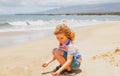 Cute boy playing with sand on summer tropical beach. Happy kid sit on the seaside sandy beach and playing with sand.