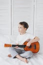 Boy playing a small guitar sitting on the bed Royalty Free Stock Photo