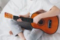 Boy playing a small guitar sitting on the bed Royalty Free Stock Photo