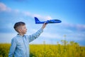 Cute boy plays with a toy airplane in the the blue sky and dreams of travel. Hand with blue toy plane Royalty Free Stock Photo