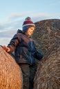 A cute boy poses on top of a pile of straw bales, sunset lights, a background of blue sky Royalty Free Stock Photo