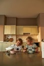 Cute boy pouring milk into a bowl of cereal while preparing breakfast, sitting together with his little sister at the Royalty Free Stock Photo