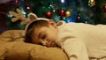 Cute boy pretends to sleep in front of christmas tree trying to catch Santa Claus when he comes to leave gifts.