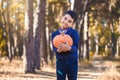 Cute boy with a pumpkin in his hands in a pine forest