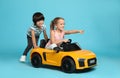 Cute boy pushing children`s electric toy car with little girl on light blue background