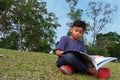 A cute boy reading a book in a park seriously