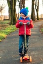 Cute boy riding on his scooter in the local park. Kid wears colorful jacket, hat and gloves. Autumn fashion. Happy playtime