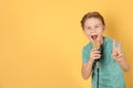 Cute boy singing in microphone on color background Royalty Free Stock Photo