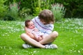 Cute boy sitting in a beautiful summer garden full with flowers holding his newborn sister