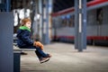 Cute boy, sitting on a bench with teddy bear, looking at a train Royalty Free Stock Photo