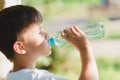 Cute boy sitting on the grass drinks water from a bottle in the summer at sunset. Child quenches thirst on a hot day Royalty Free Stock Photo