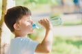 Cute boy sitting on the grass drinks water from a bottle in the summer at sunset. Child quenches thirst on a hot day Royalty Free Stock Photo