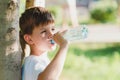 Cute boy sitting on the grass drinks water from a bottle in the summer at sunset. Child quenches thirst on a hot day Royalty Free Stock Photo