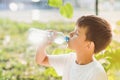 Cute boy sitting on the grass drinks water from a bottle in the summer at sunset. Child quenches thirst on a hot day Royalty Free Stock Photo