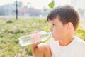 Cute boy sitting on the grass drinks water from a bottle in the summer at sunset. Child quenches thirst on a hot day Royalty Free Stock Photo