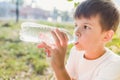 Cute boy sitting on the grass drinks water from a bottle in the summer at sunset. Child quenches thirst on a hot day Royalty Free Stock Photo