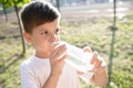 Cute boy sitting on the grass drinks water from a bottle in the summer at sunset. Child quenches thirst on a hot day Royalty Free Stock Photo