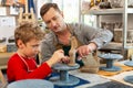 Cute boy sitting near his teacher sculpting little clay animal