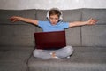 Cute boy sitting on a sofa with headphones and having fun chatting on a notebook. Little cute boy with laptop at home.