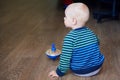 Cute boy in a striped sweater plays with whirligig on the floor, back view Royalty Free Stock Photo