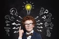 Cute boy student pointing up and looking at lightbulb on blackboard background. Idea concept Royalty Free Stock Photo