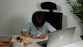 cute boy studying online at his desk. writes assignments in a note and looks at the laptop screen