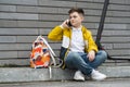 Cute boy talking on the phone while sitting on the sidewalk near his electric scooter.