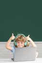 Cute boy with thumbs up wearing headphones, study with laptop in classroom, listening audio lesson course. First day at Royalty Free Stock Photo