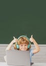 Cute boy with thumbs up wearing headphones, study with laptop in classroom, listening audio lesson course. First day at Royalty Free Stock Photo