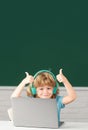 Cute boy with thumbs up wearing headphones, study with laptop in classroom, listening audio lesson course. First day at Royalty Free Stock Photo