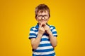 Cute boy wearing glasses and blue striped polo, touching chin with both index finger against yellow Royalty Free Stock Photo