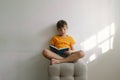 A cute boy wearing an orange T-shirt is sitting on a soft ottoman reading a book